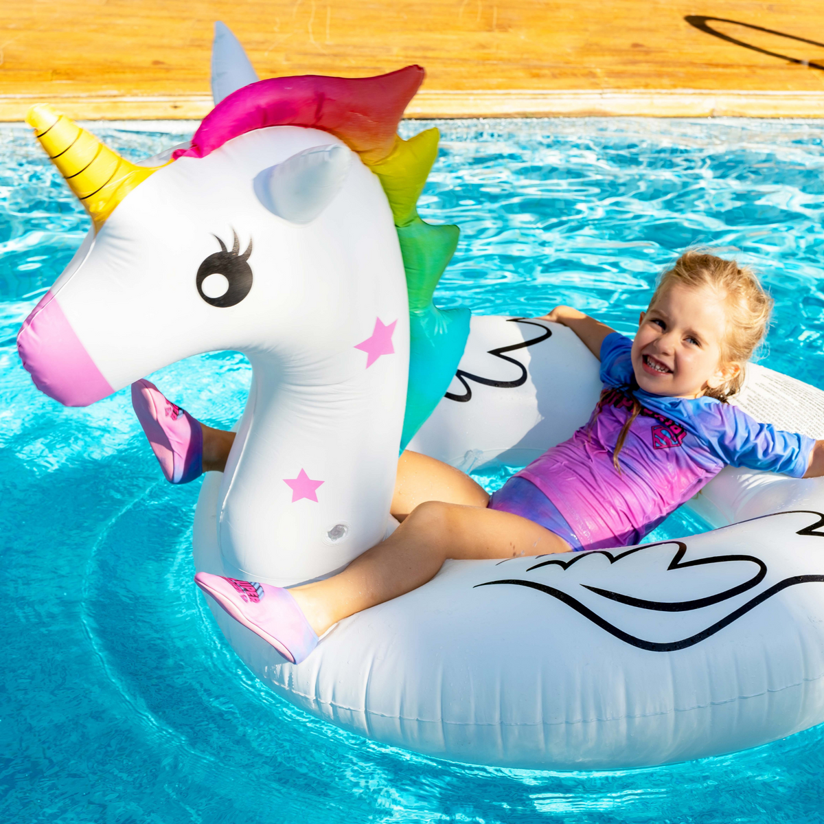 Child on a unicorn inflatable pool float in a swimming pool, wearing slipstop shoes and swimwear